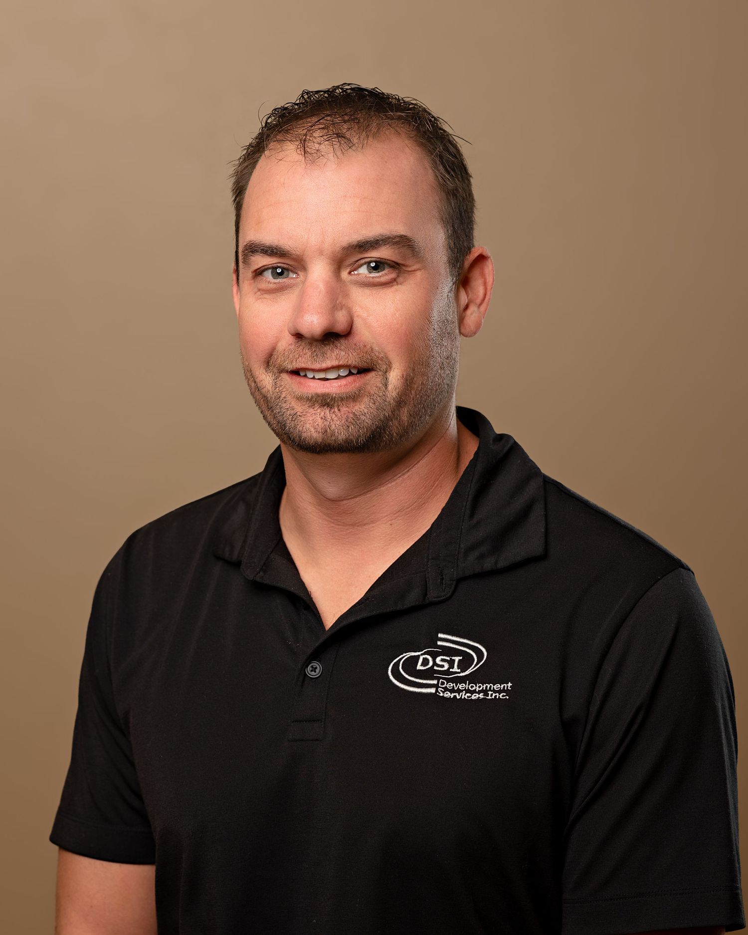 Professional headshot of man with short brown hair wearing black DSL company polo shirt.