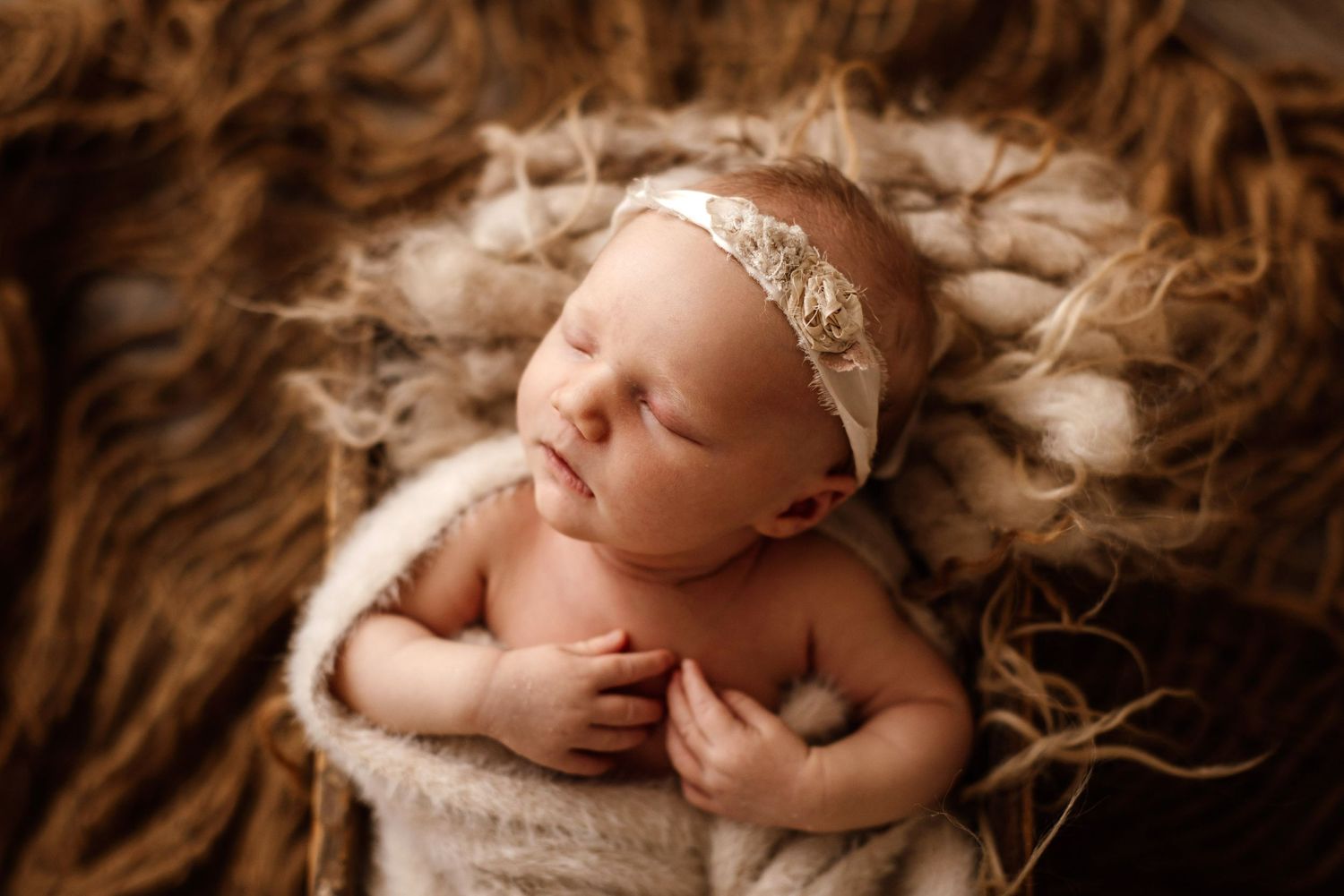 Sleeping newborn photographed in sepia tones with soft fur and delicate textures.