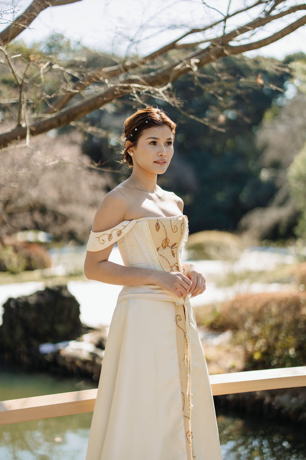 Elegant off-shoulder cream dress captured in natural outdoor garden setting.