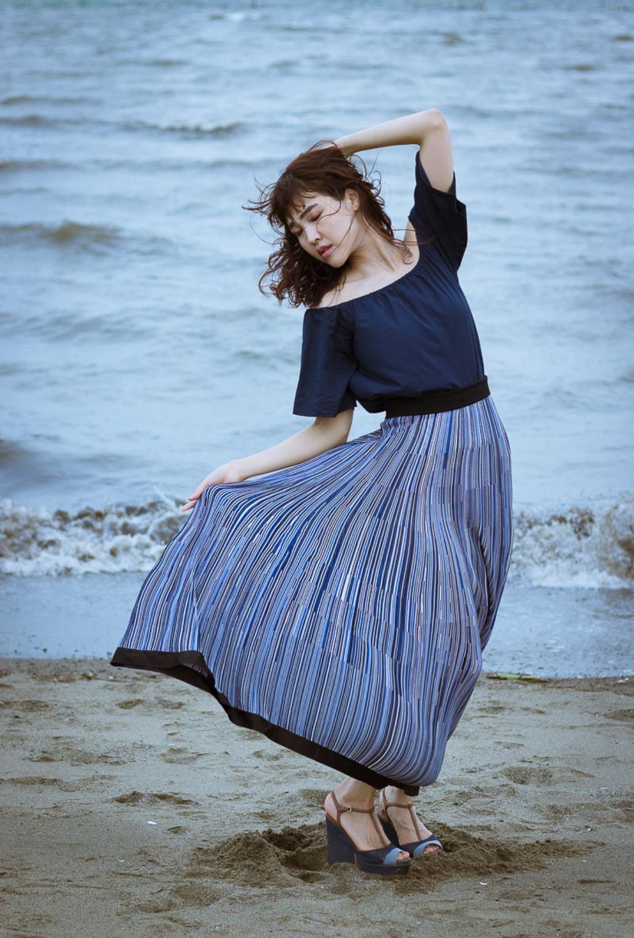 Dancing figure in striped skirt twirls gracefully on beach at dusk.