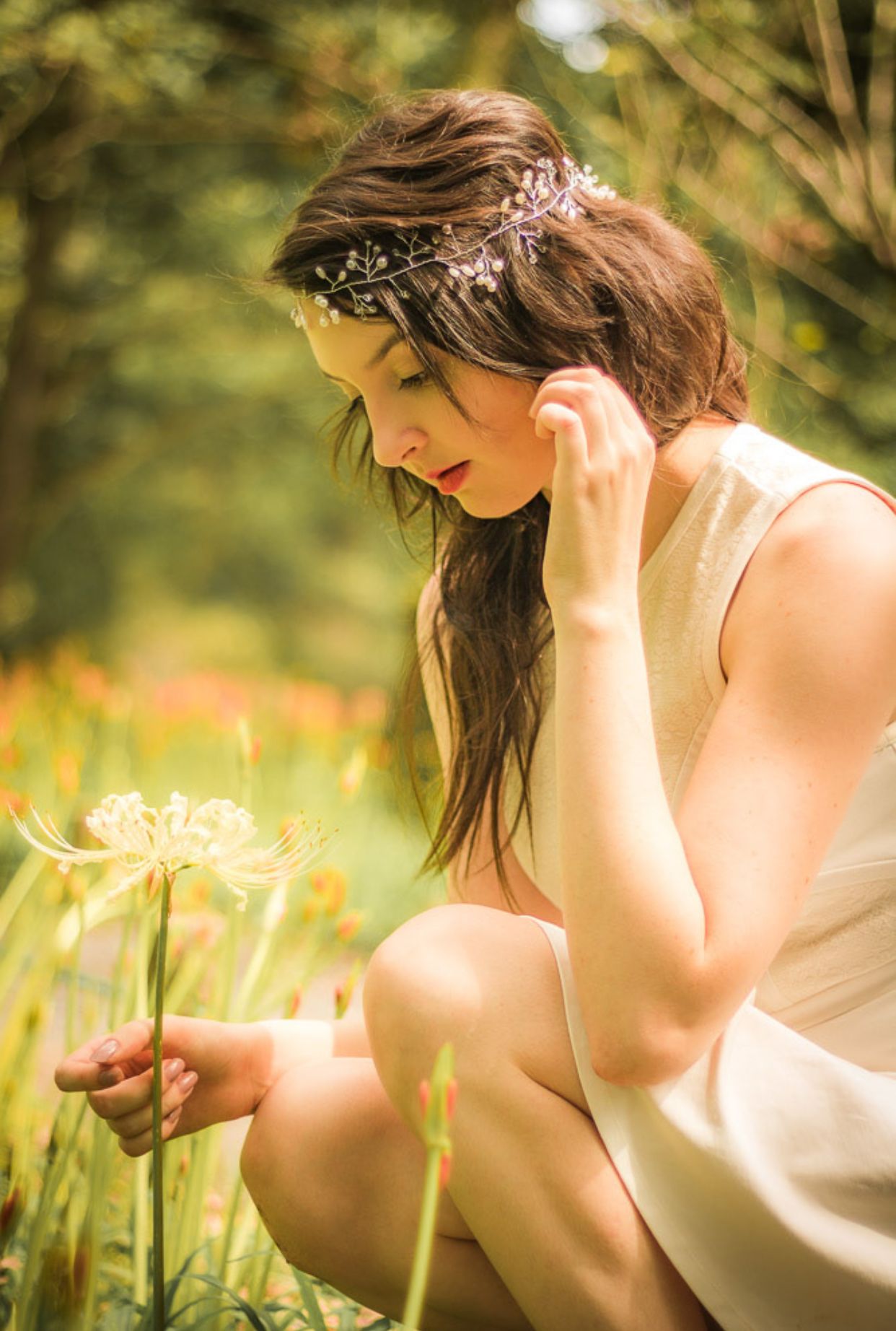 Dreamy summer portrait with floral headpiece examining flower in sunny meadow.