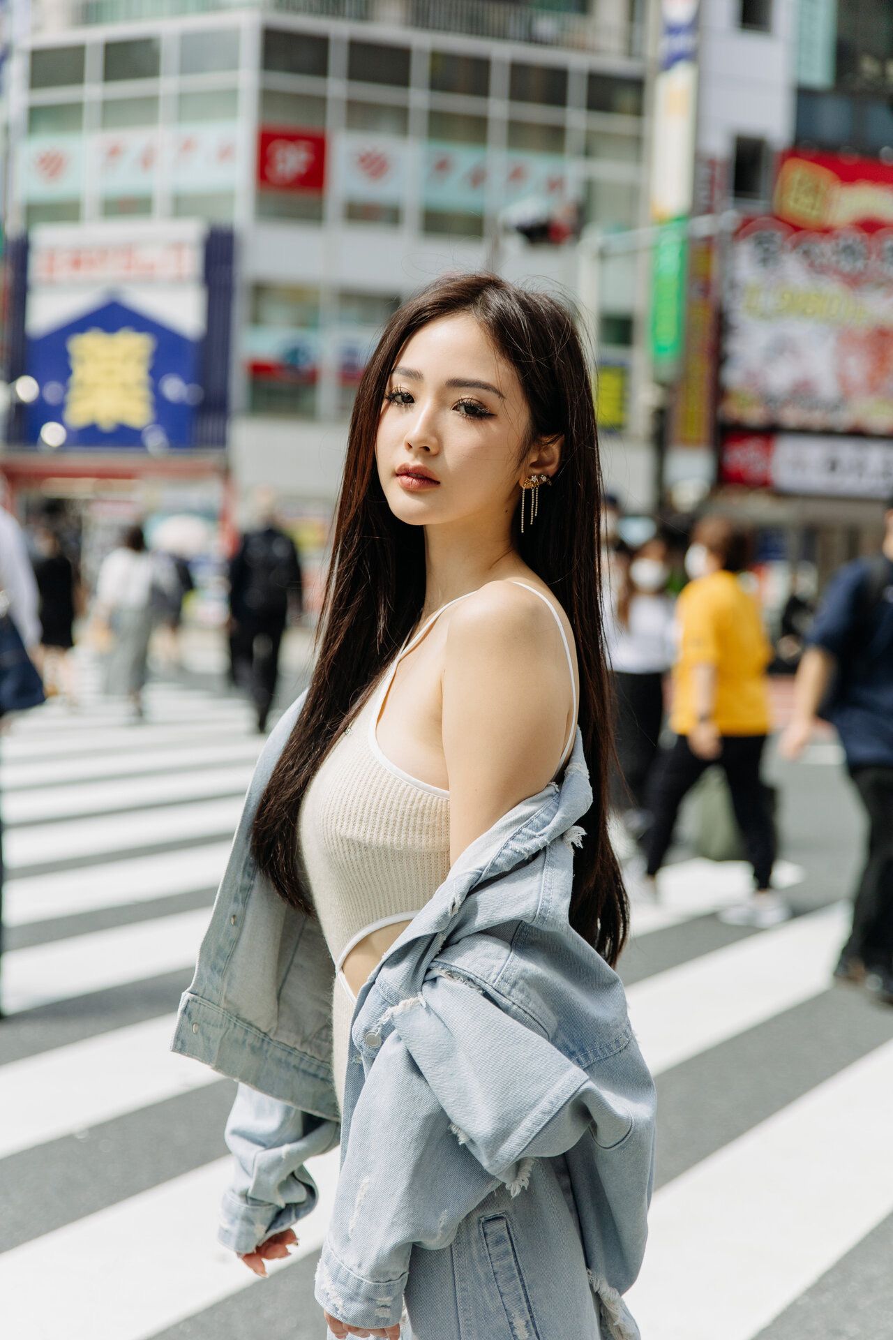 Streetwear fashion photography in urban Tokyo with denim jacket and white top against city backdrop.