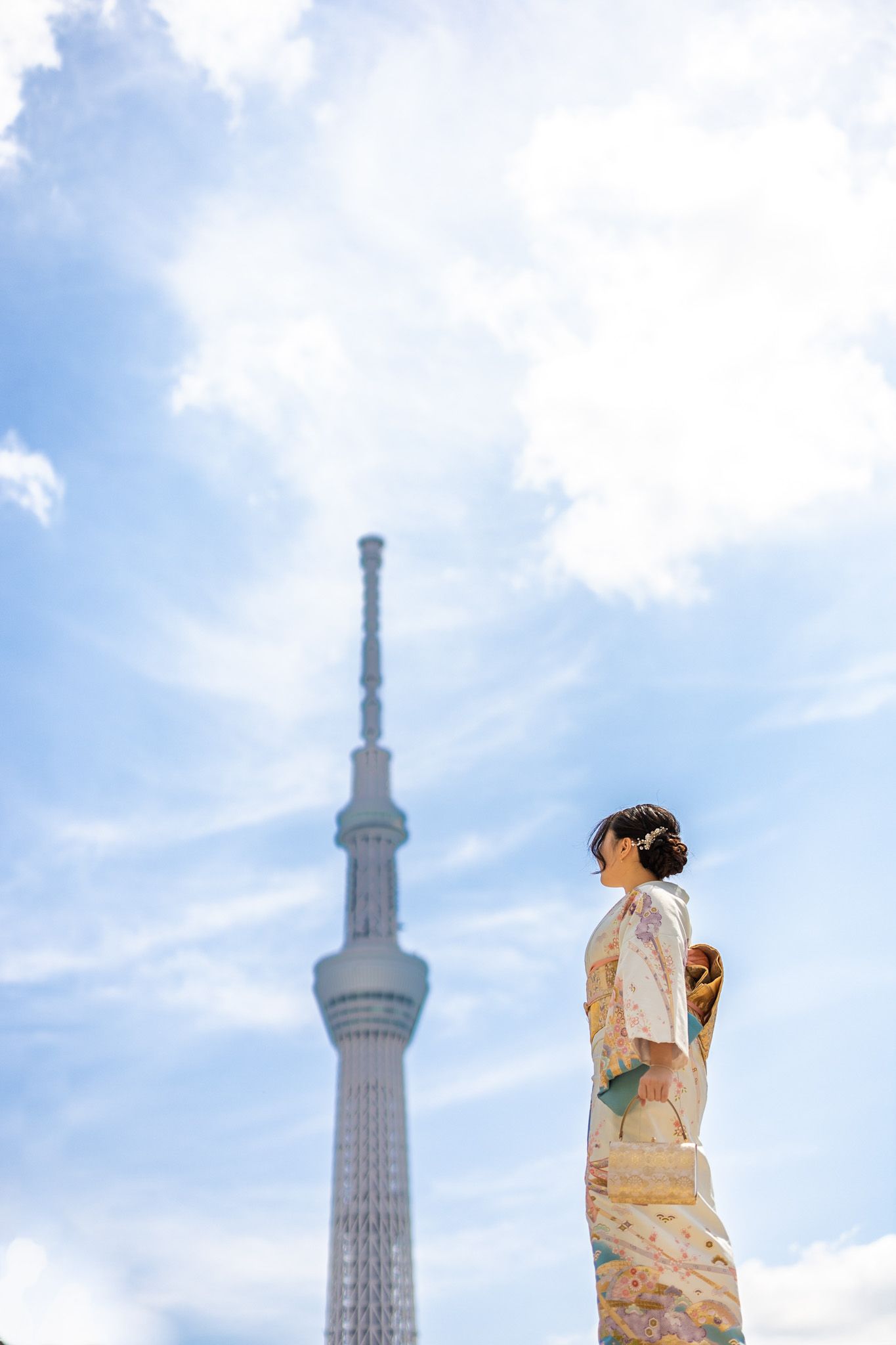 Person in traditional kimono looking at Tokyo Skytree tower against blue sky with clouds.