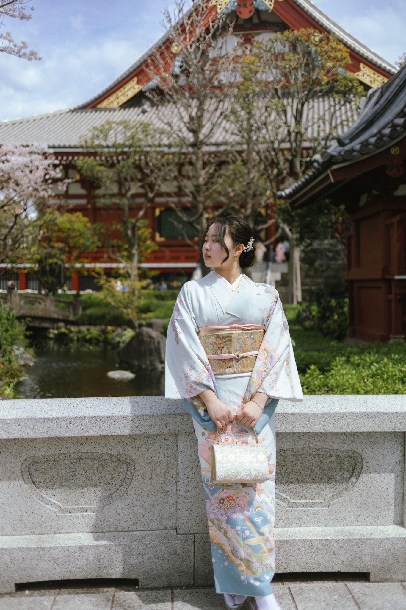 Person wearing light blue kimono standing at temple bridge with traditional architecture.