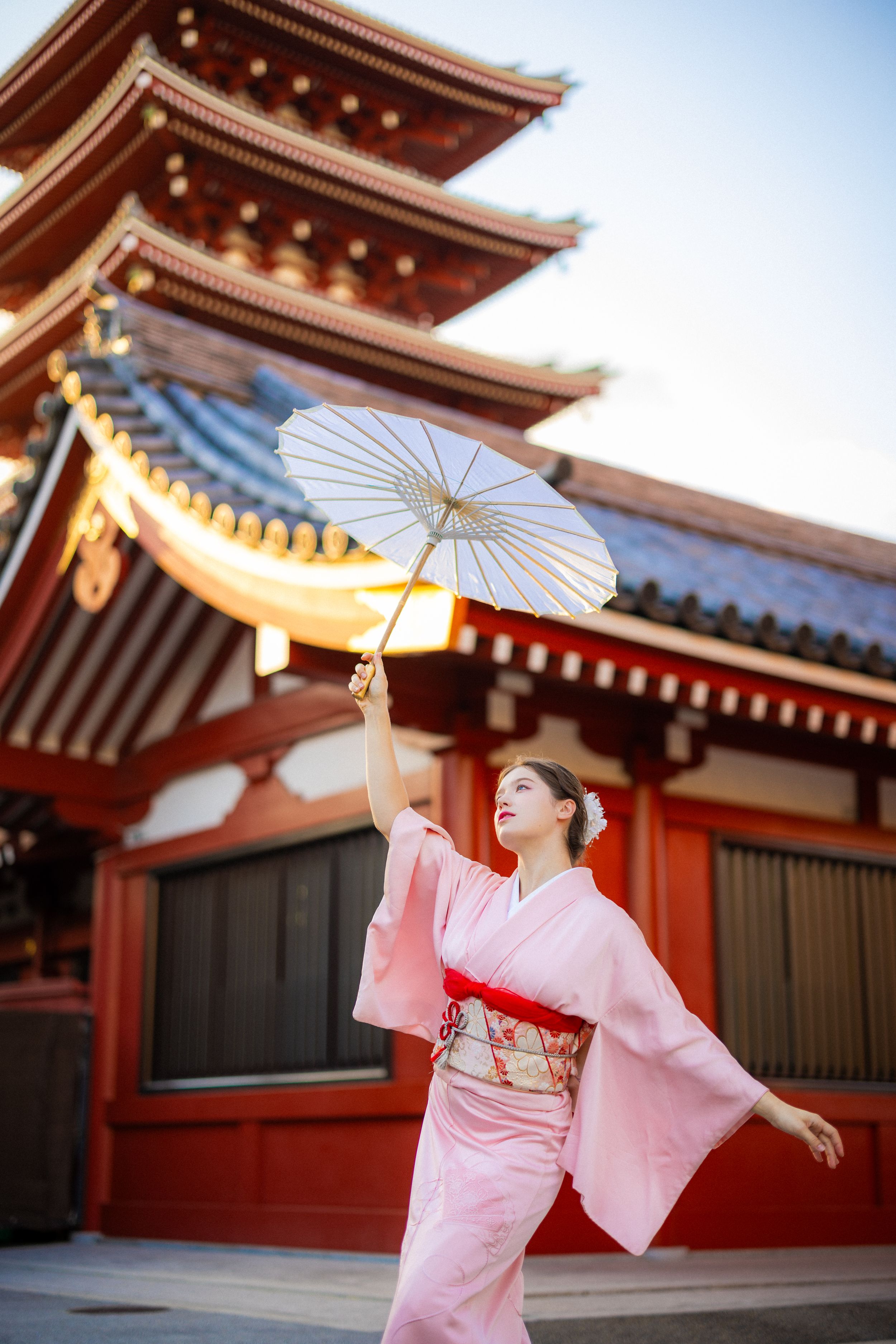 Pink kimono and white parasol against red temple architecture in Japan.