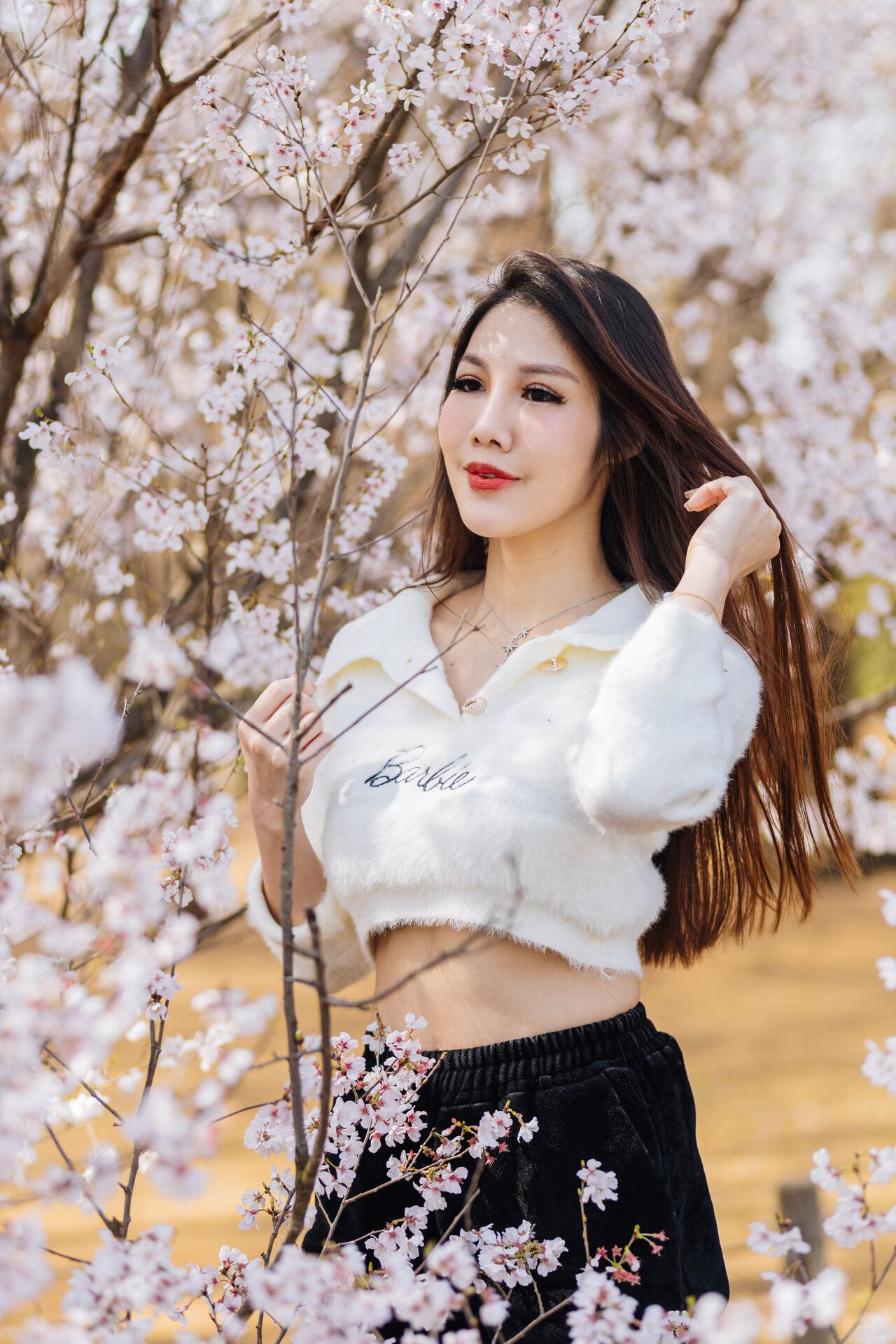 Woman in white crop top poses among blooming cherry blossoms.