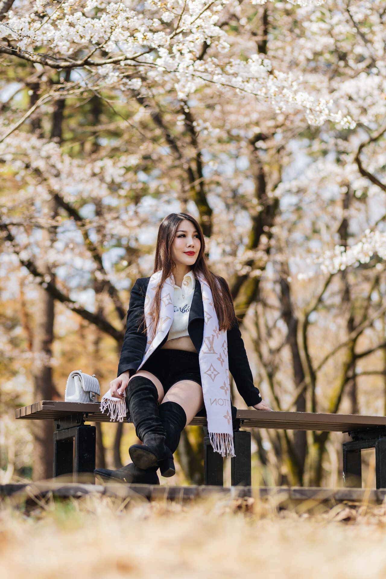 Woman sitting on wooden bench surrounded by blooming cherry trees.