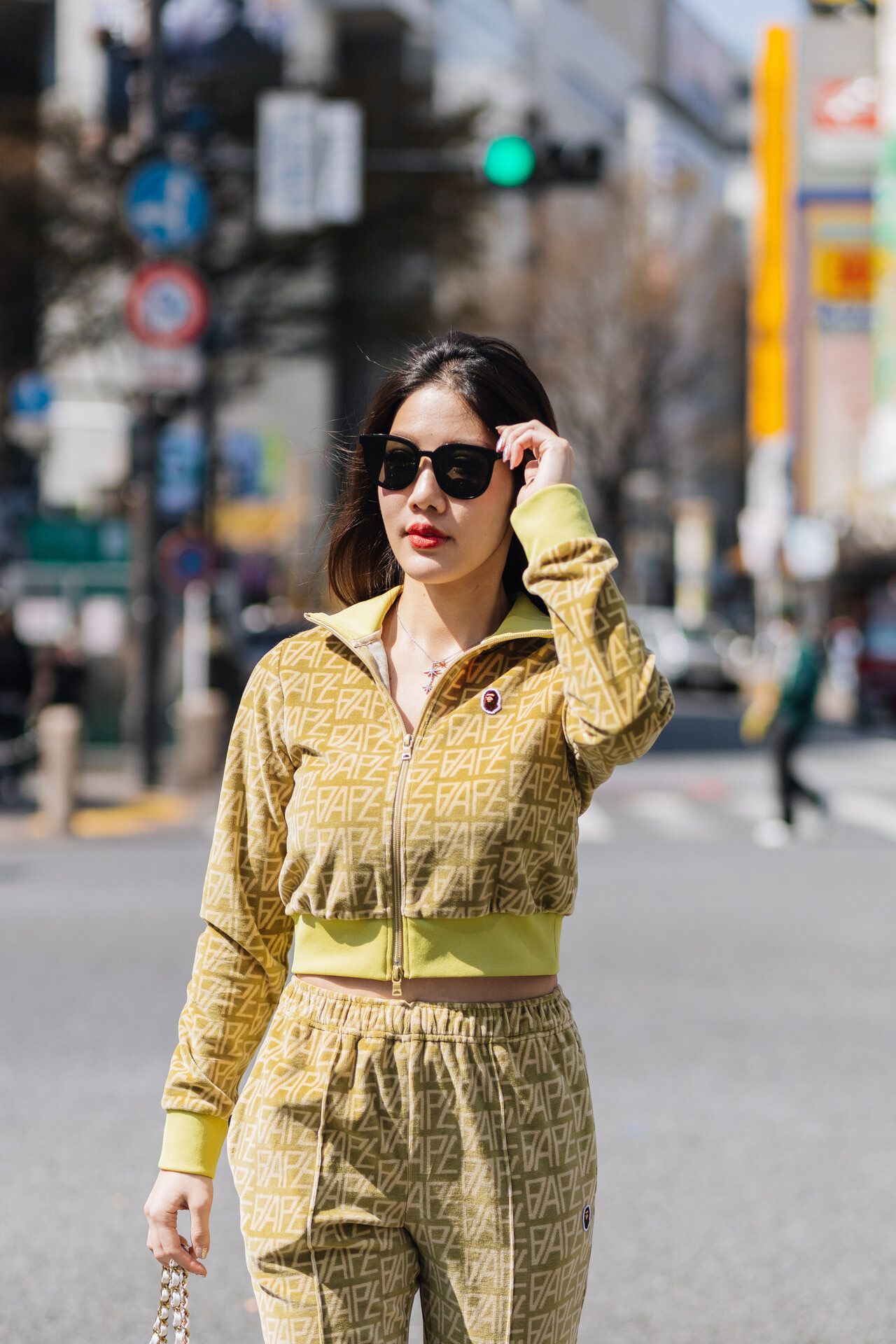 Woman in yellow tracksuit walking on urban street with sunglasses.