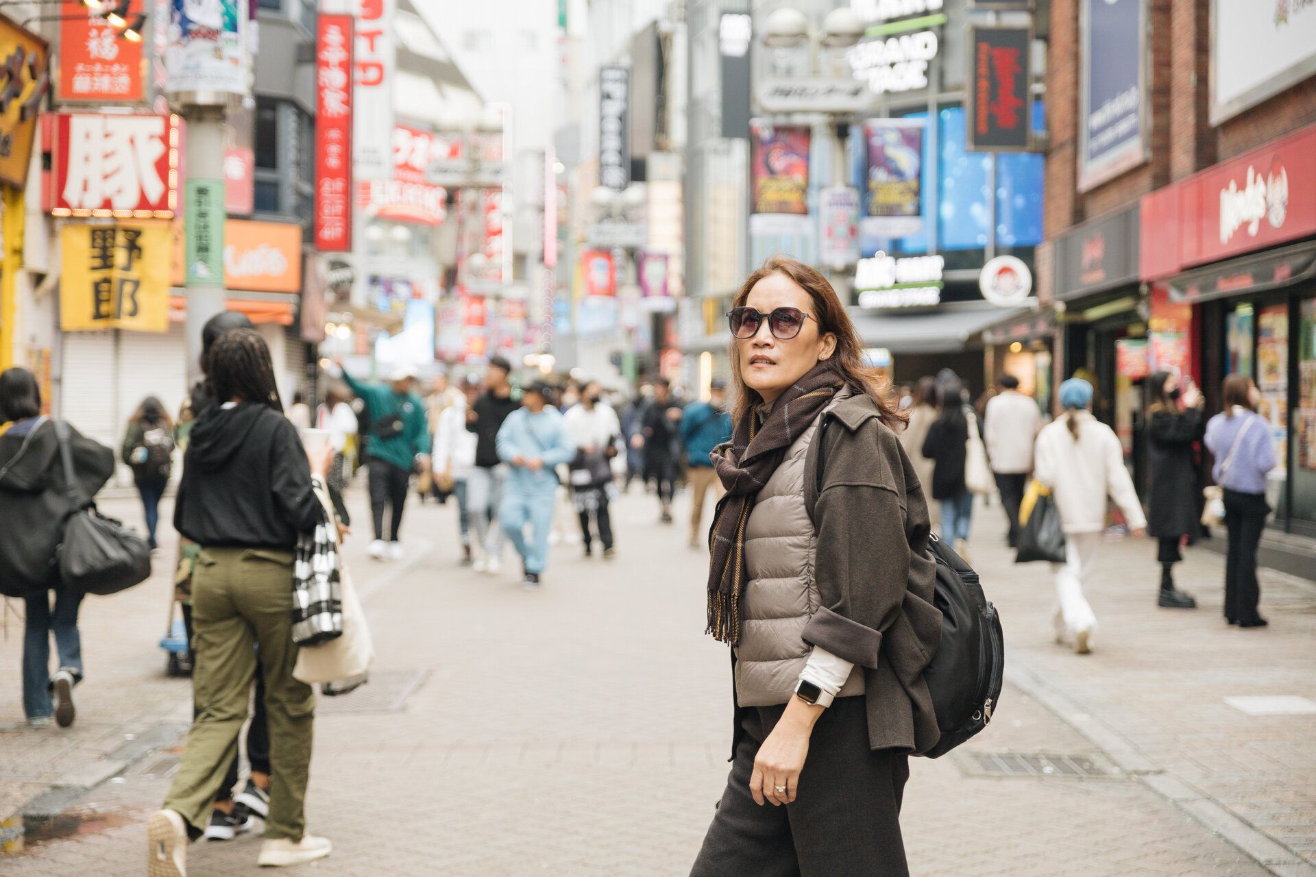 Person exploring busy shopping district with backpack in urban Japan.