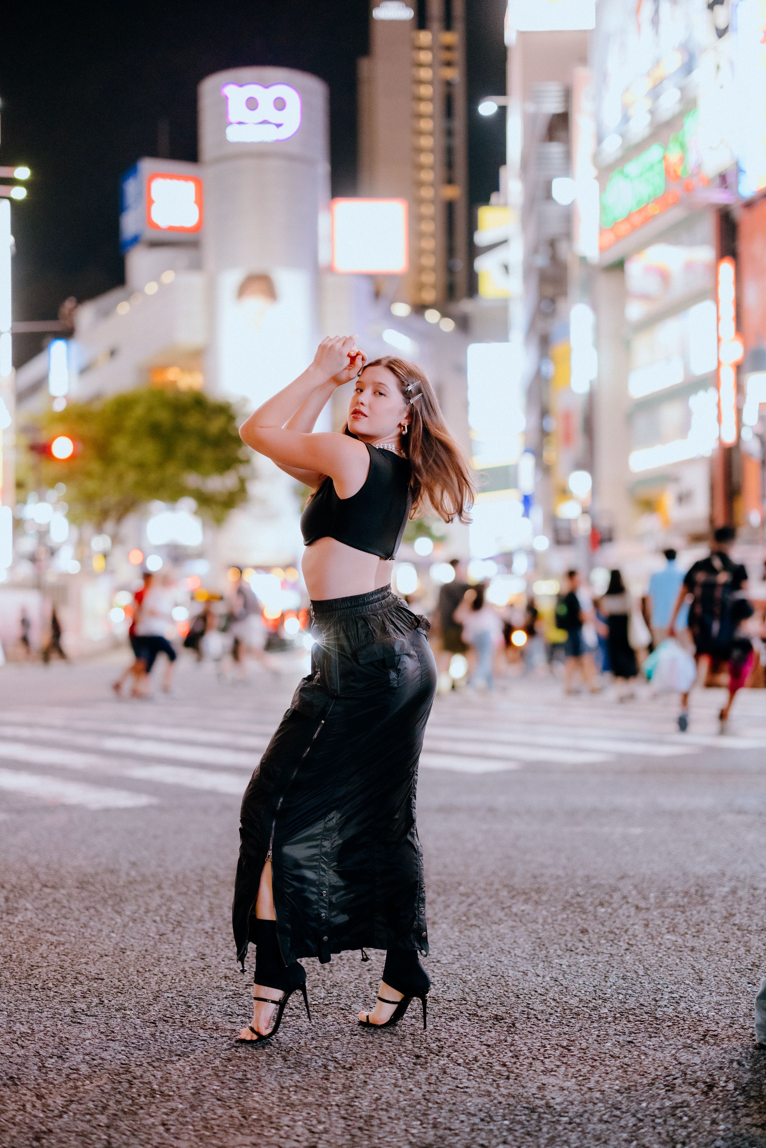 Urban fashion portrait on bustling Tokyo street crossing at night.