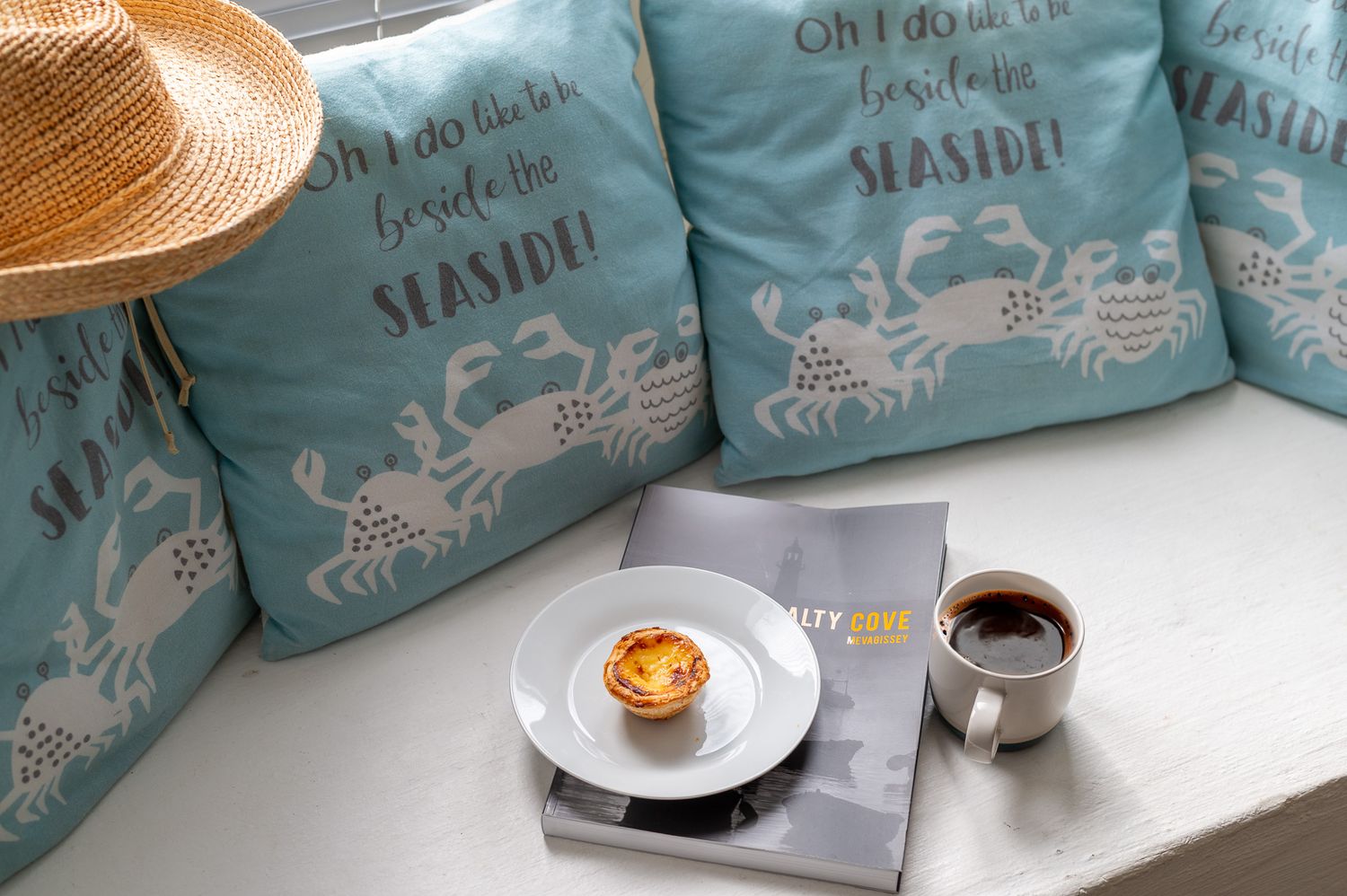mevagissey holiday let review with image of coffee and pastel de nata, relaxing vibe with blue cushions and straw hat