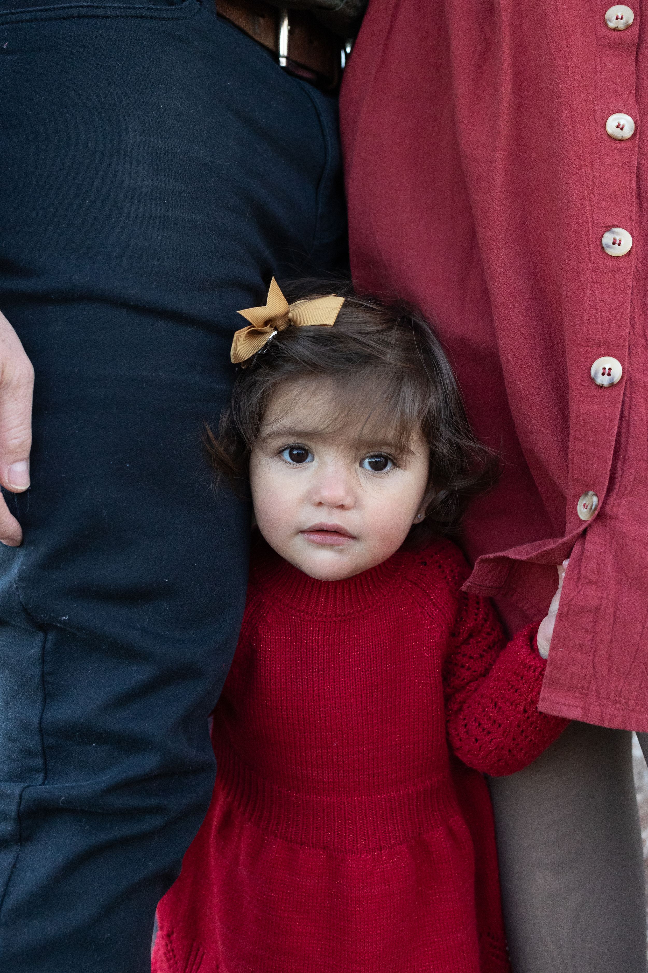 Small child in red dress standing between two adults wearing navy and burgundy clothing.