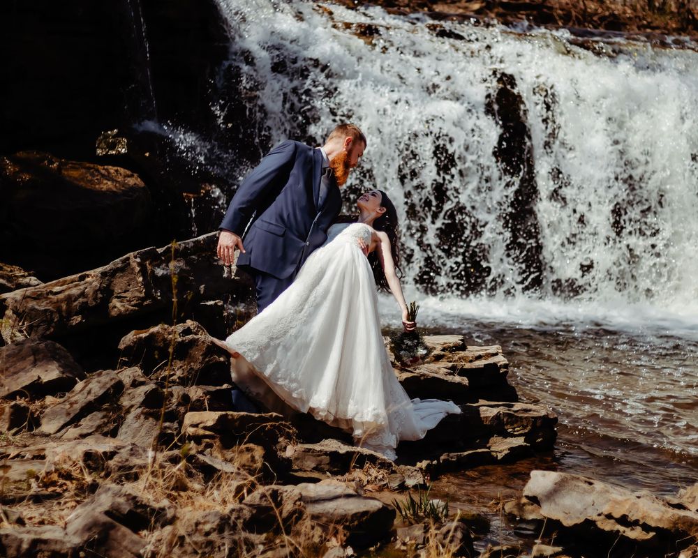 Romantic wedding pose on rocky waterfall landscape.
