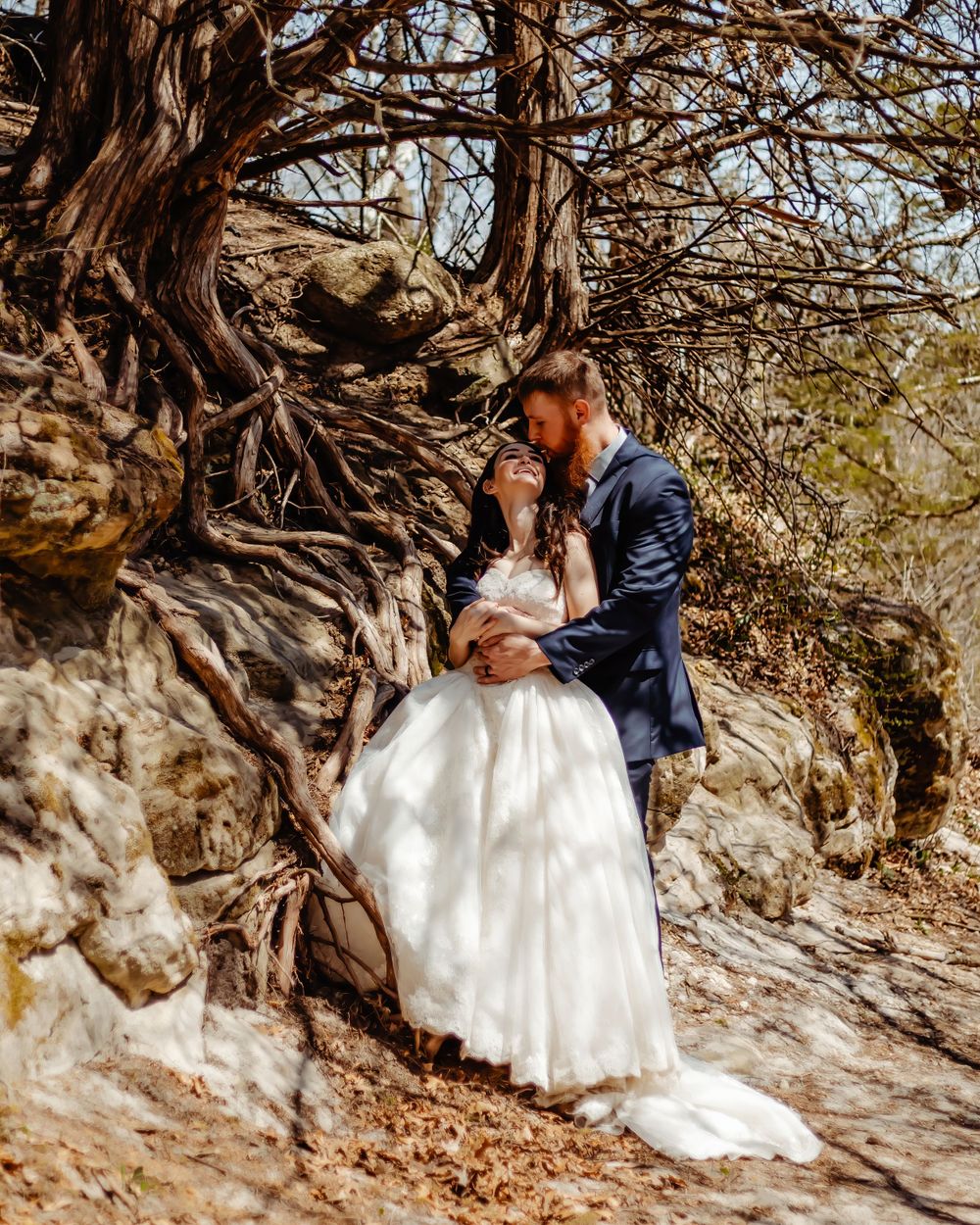 A tender wedding moment photographed against twisted tree roots and rocky cliffs.