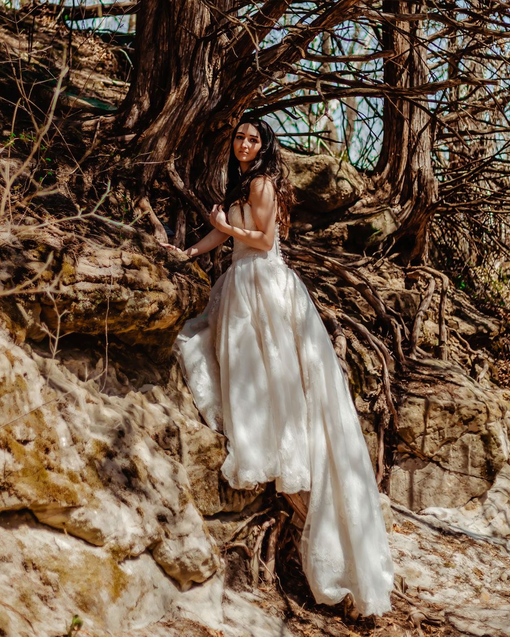 White wedding dress flowing beautifully against natural rock formations and twisted tree roots.