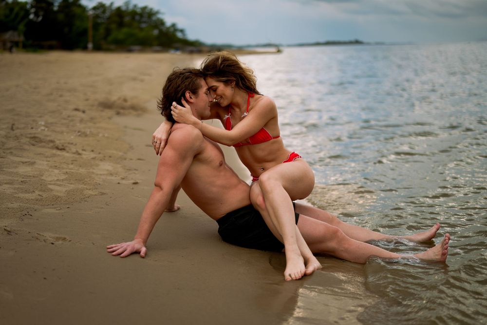 Two people enjoying a romantic moment sitting together on a sandy tropical beach at sunset.