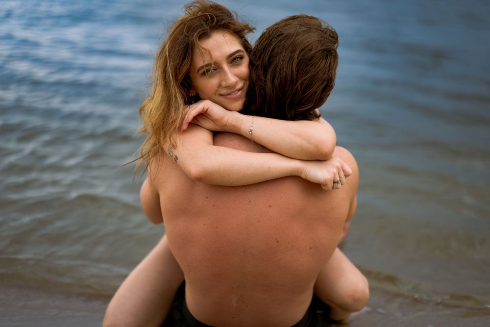 A couple embraces while standing in shallow ocean water during a romantic moment at the beach.