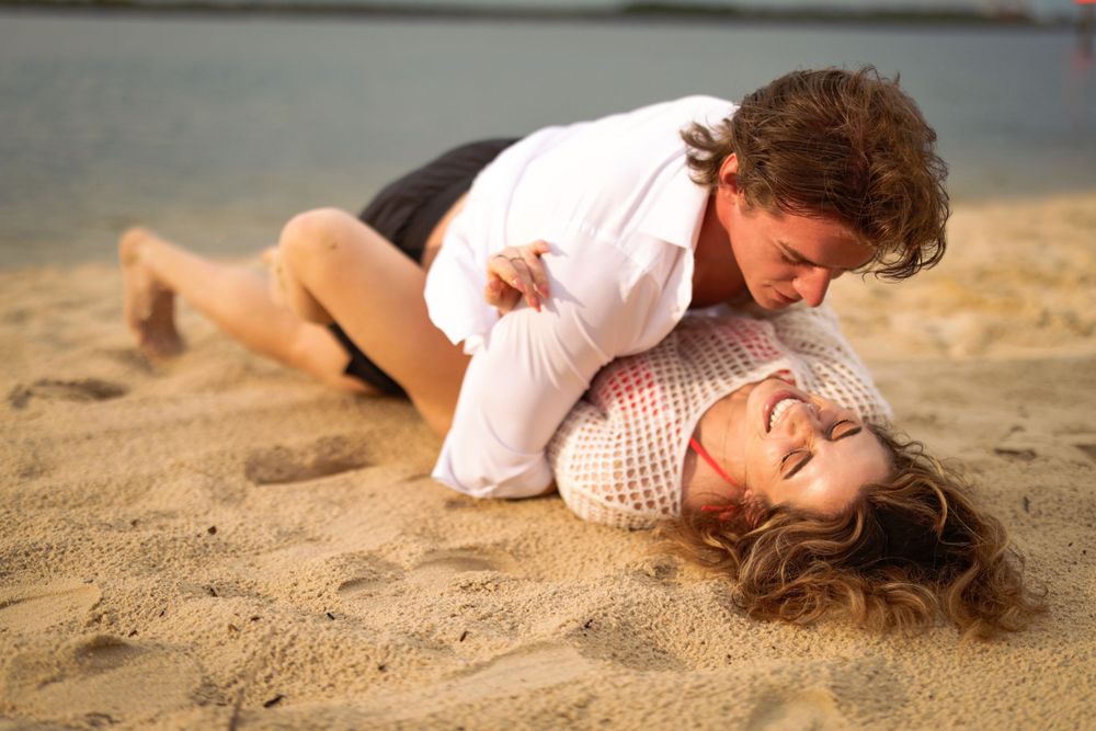 Playful interaction between parent and child on a sandy beach during golden hour lighting.