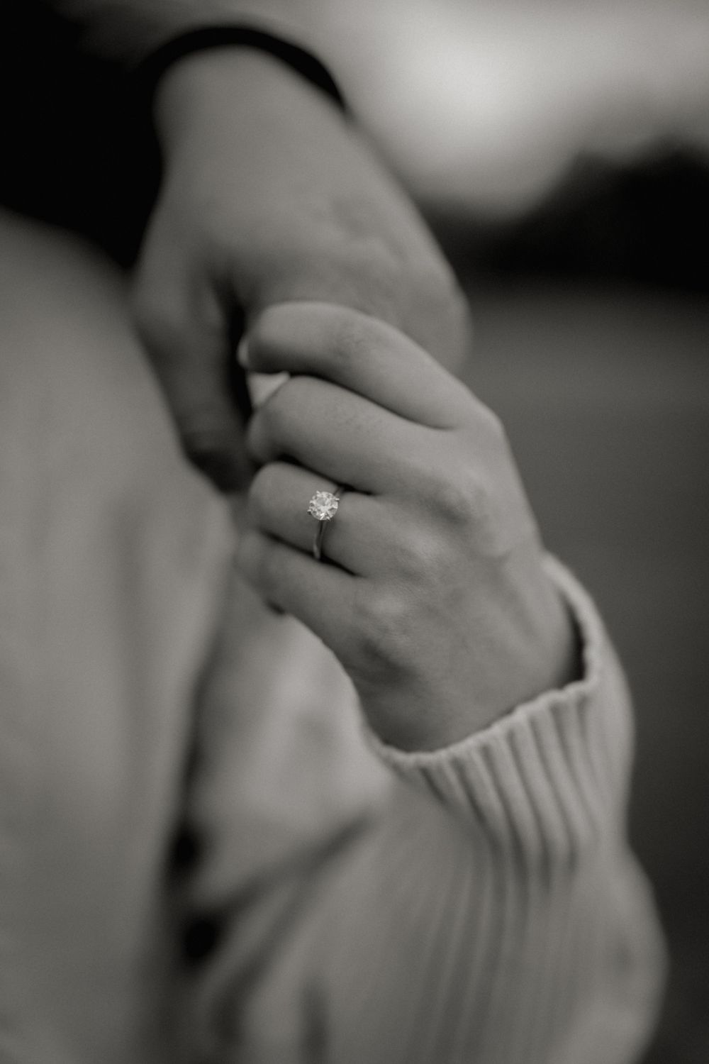 Close-up view of hands wearing an elegant engagement ring with a delicate diamond solitaire on ribbed fabric.