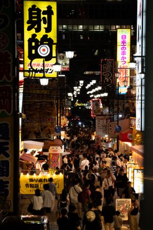 Crowded nighttime street scene in Japan with bright yellow signage and illuminated storefronts.