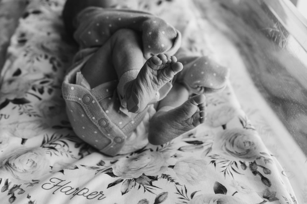 Close-up black and white photo of newborn baby feet on floral blanket.