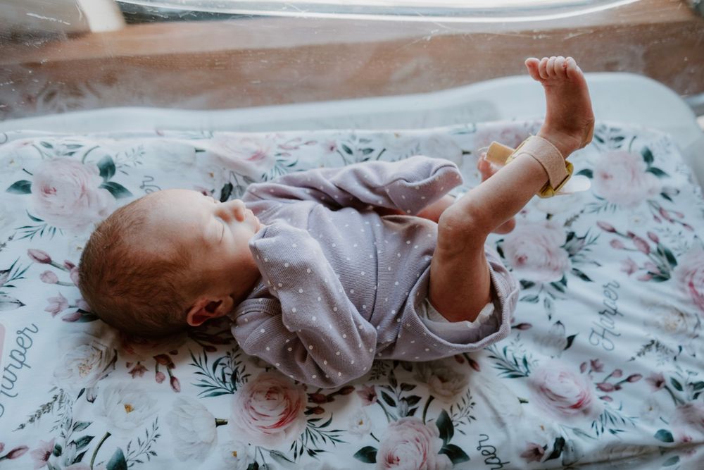Newborn baby in lavender onesie lying on a floral blanket.