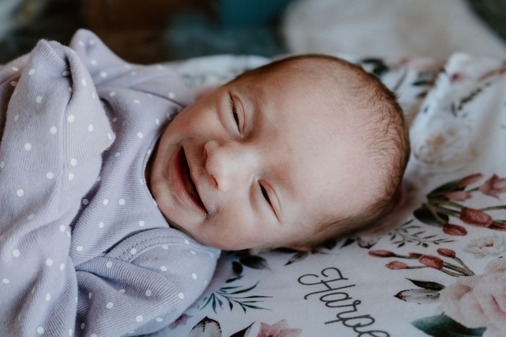Sleeping newborn baby smiling in a soft lavender swaddle blanket.