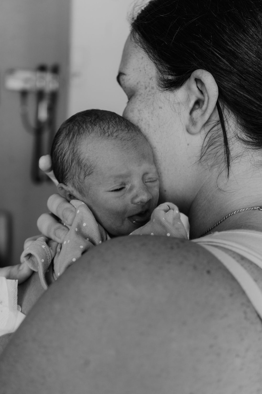 Black and white photo of a newborn baby being held close by their mother in a hospital room.