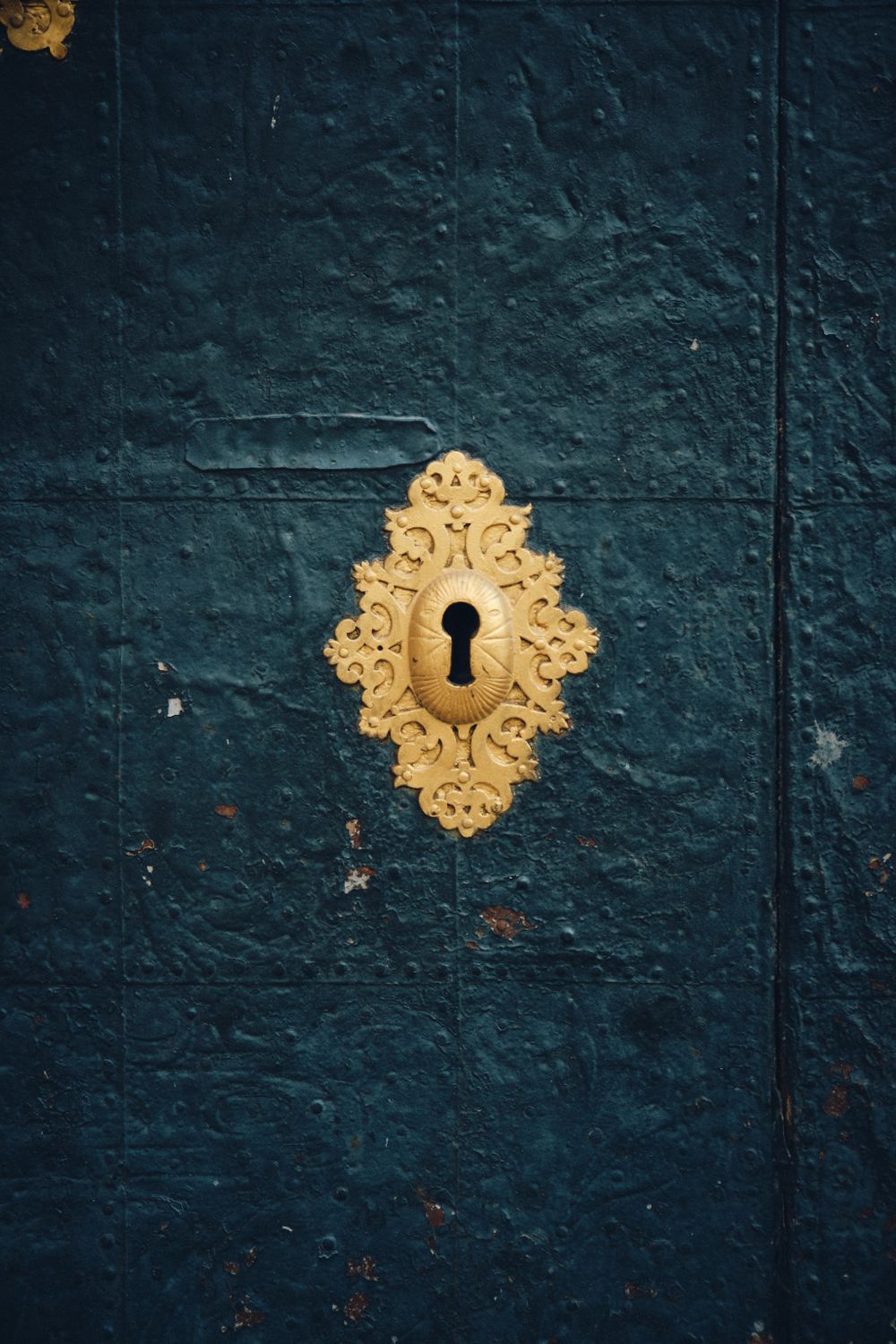 Vintage golden keyhole on textured dark teal door.