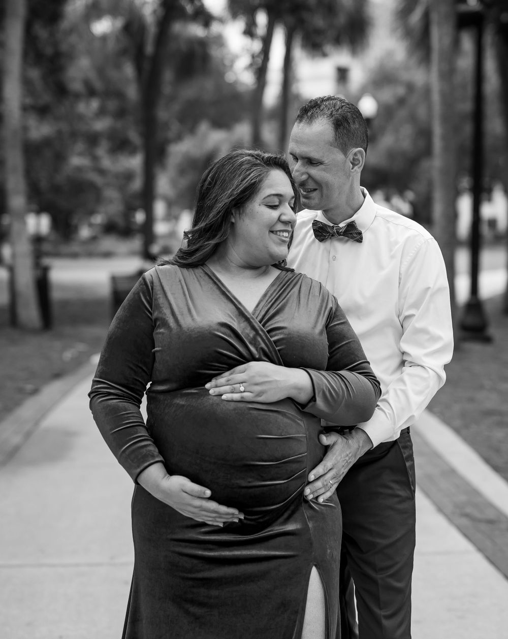 Black and white portrait of an expectant couple sharing an intimate moment outdoors.