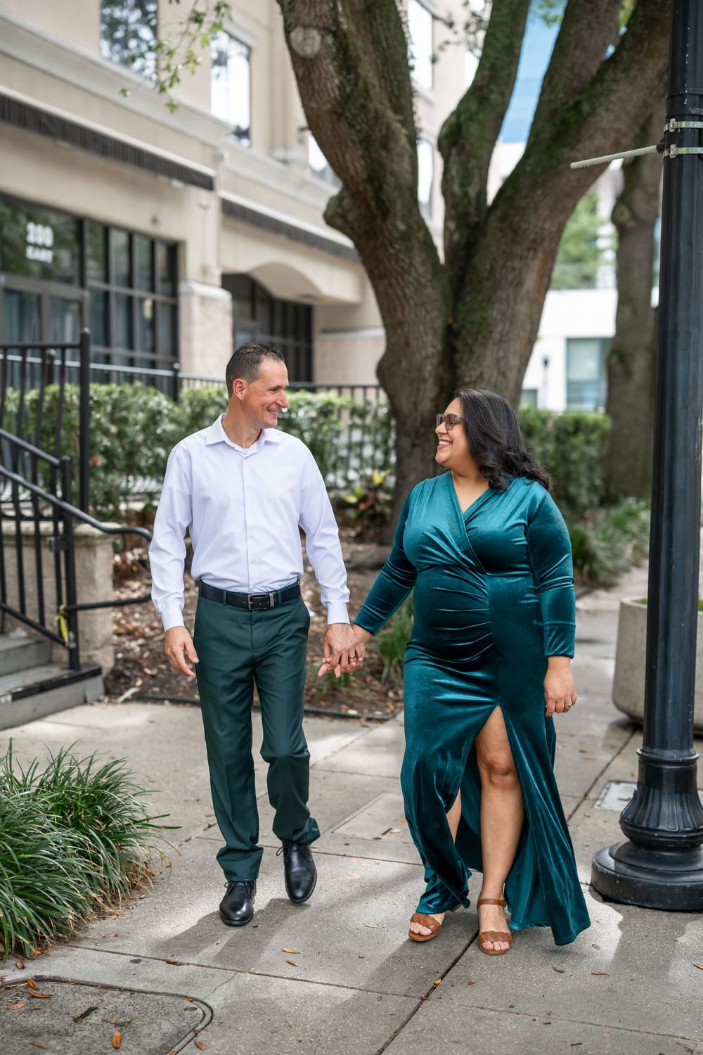 Couple walking together on a sidewalk, with the woman wearing an elegant teal evening gown.