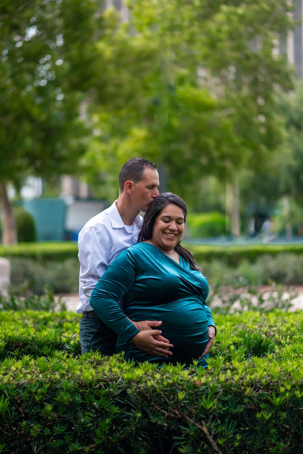 Romantic maternity photo of couple embracing in a lush garden setting.
