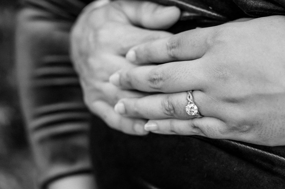 Black and white close-up of hands resting on belly showing wedding ring detail.