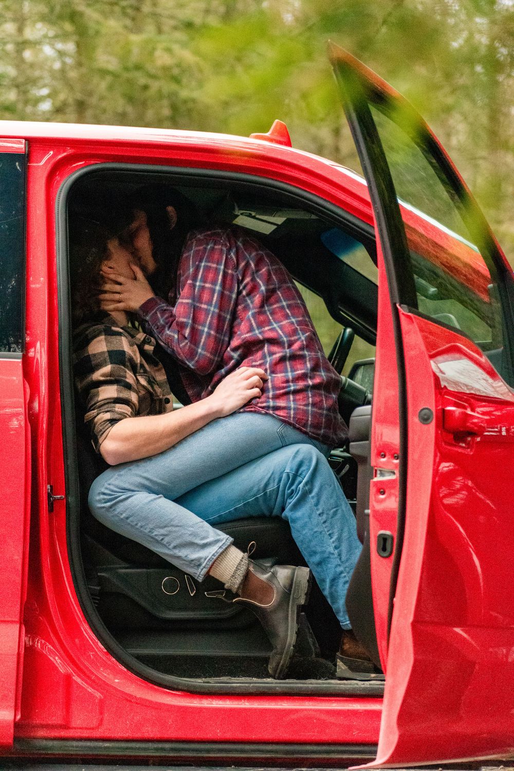 Intimate moment captured inside red truck with open door on forest road.