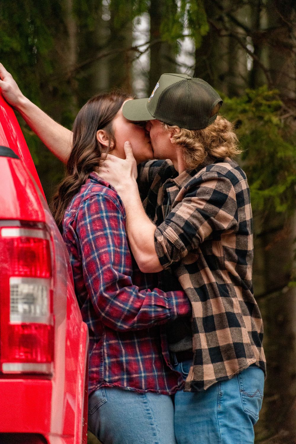 A romantic moment shared between two people wearing plaid shirts by a red truck.
