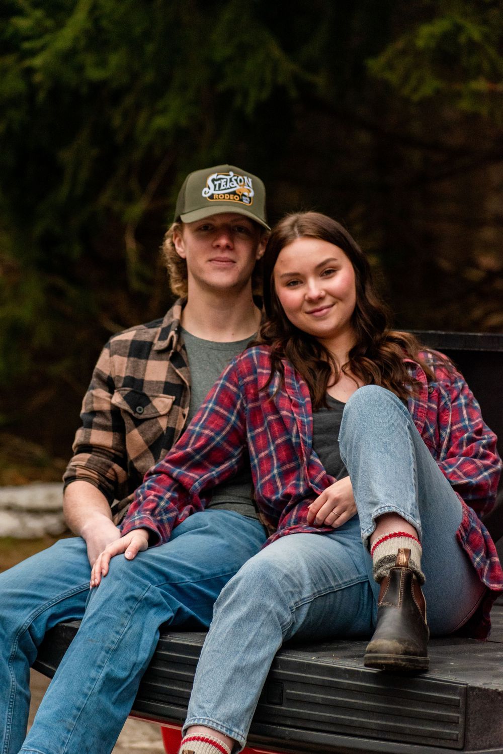 A couple in matching plaid shirts sitting on the back of a pickup truck.