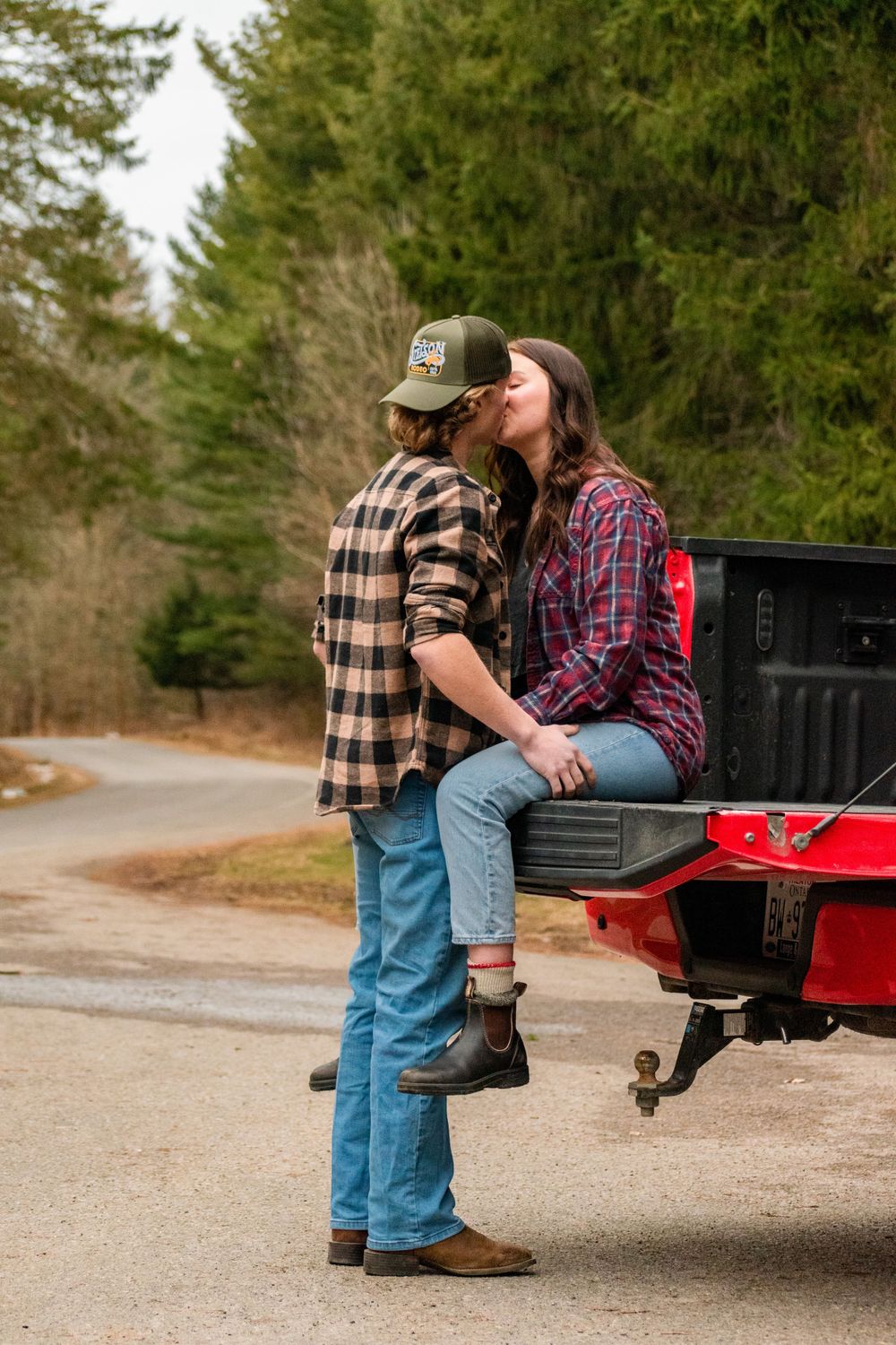 Two people in plaid shirts share a moment by a red pickup truck.