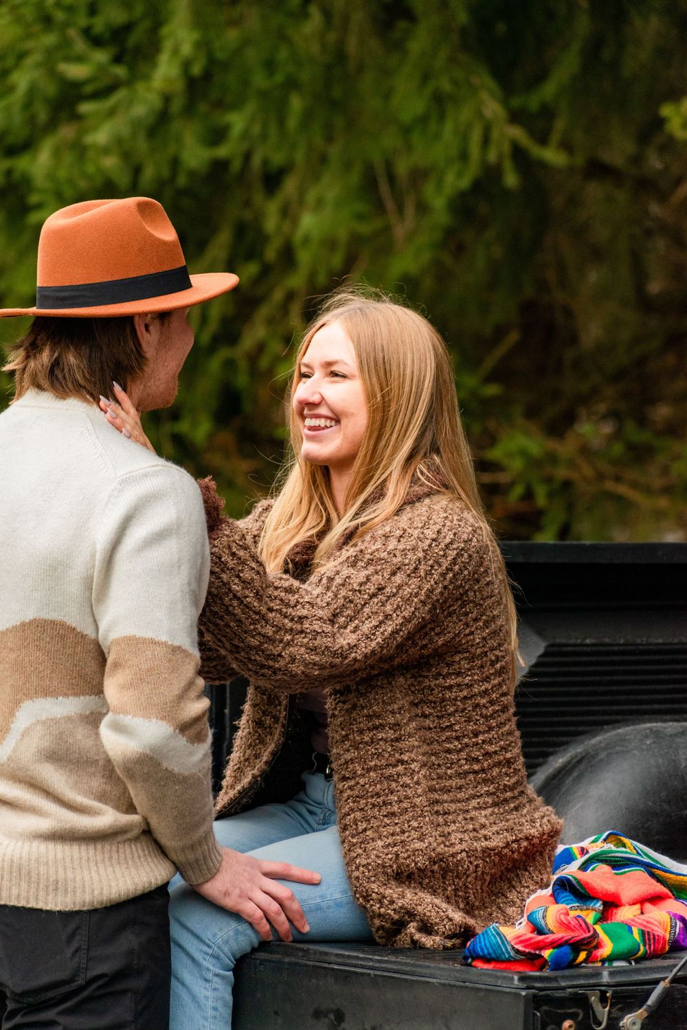 Happy moment shared between couple sitting on pickup truck bed near evergreen trees.