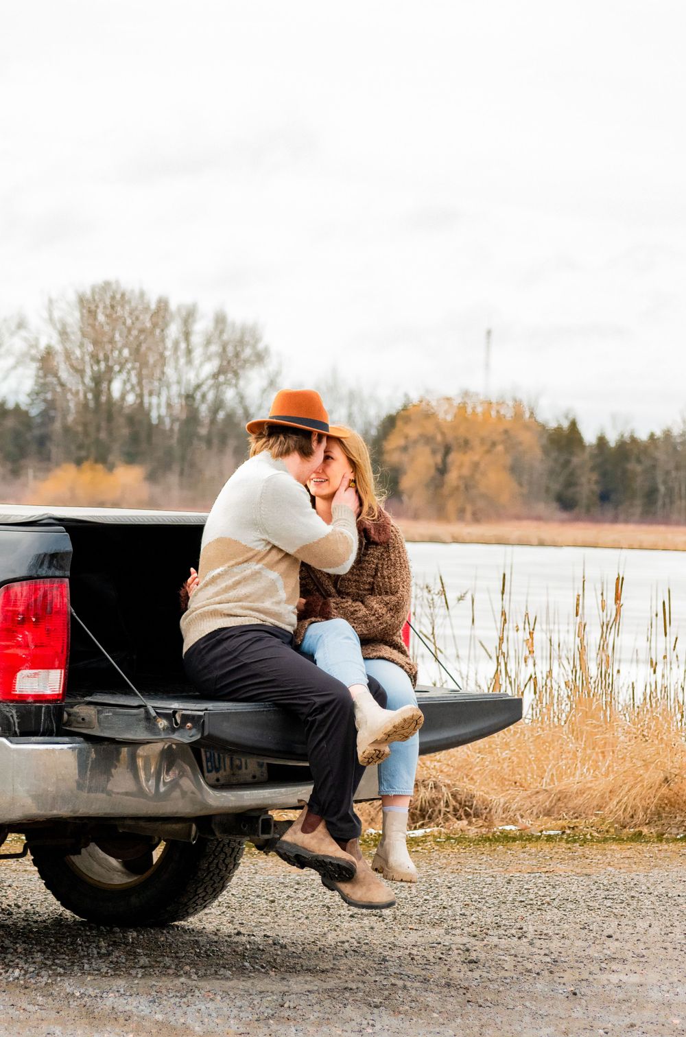 Romantic couple embracing on pickup truck tailgate by lakeside during golden hour.