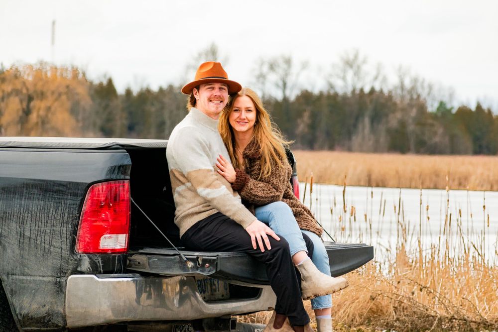 Couple enjoying autumn afternoon while sitting together on pickup truck bed near marshland.
