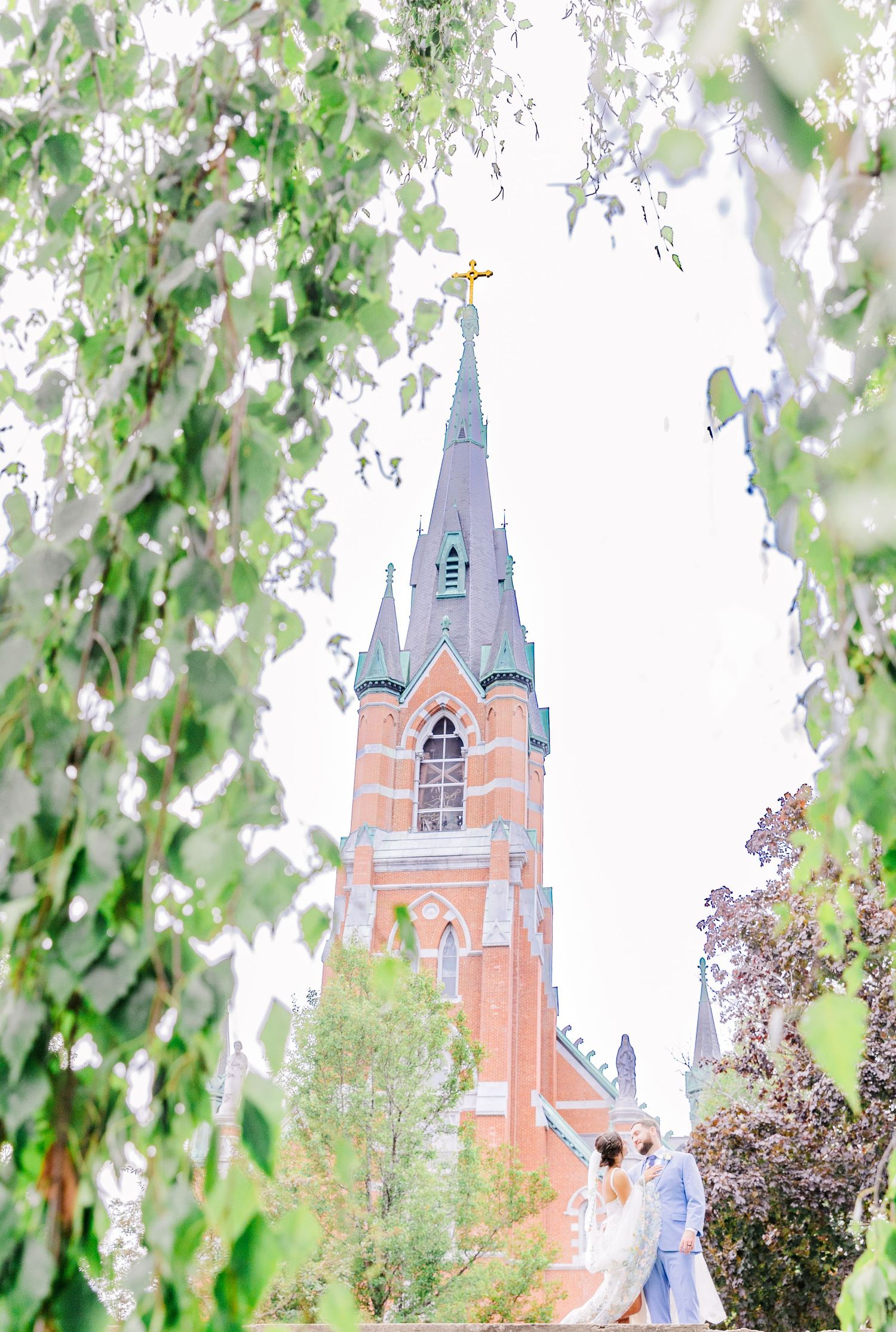 Gothic church spire framed by spring leaves creates romantic backdrop for wedding photography.