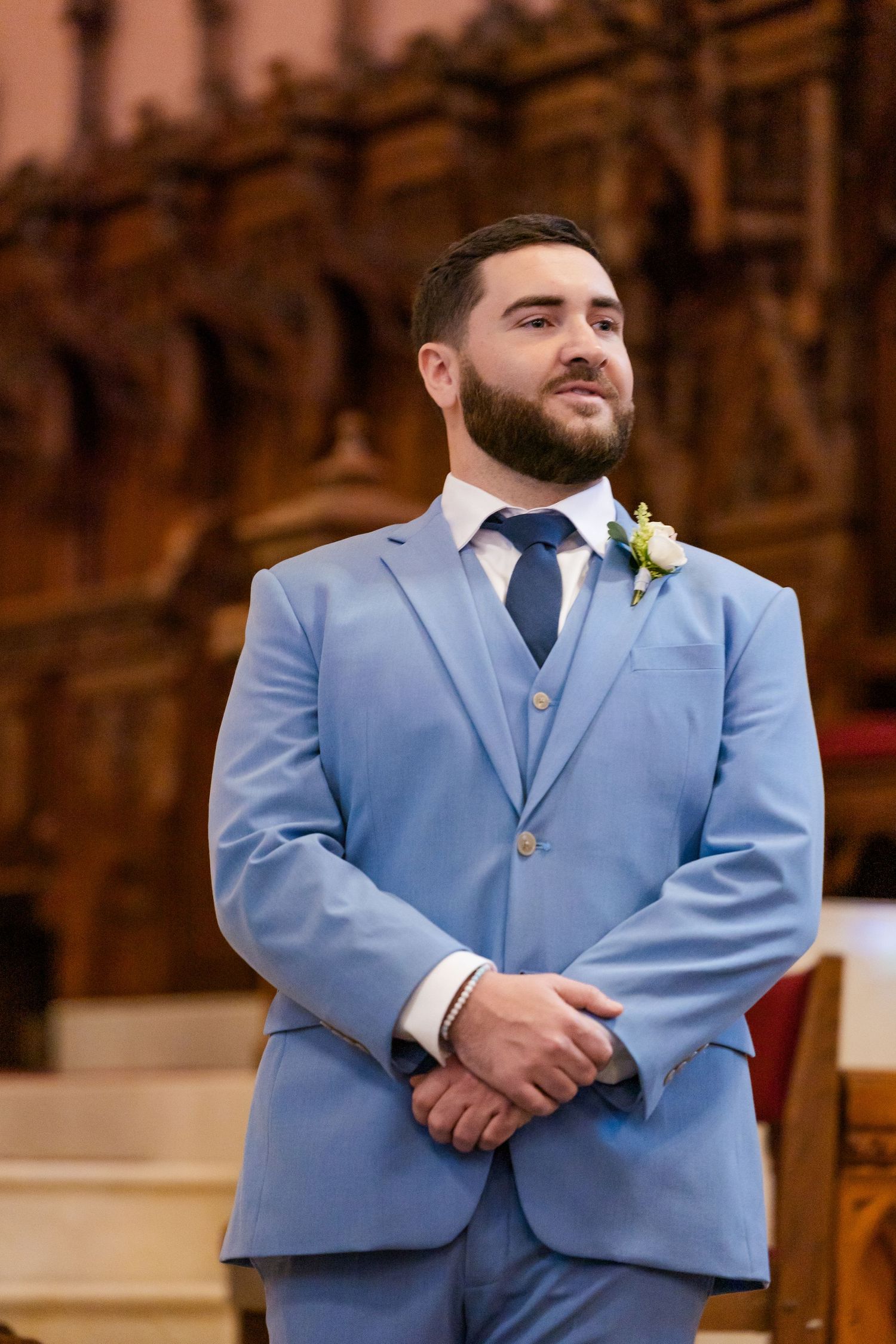 Groom in light blue three-piece suit stands at altar with boutonniere.