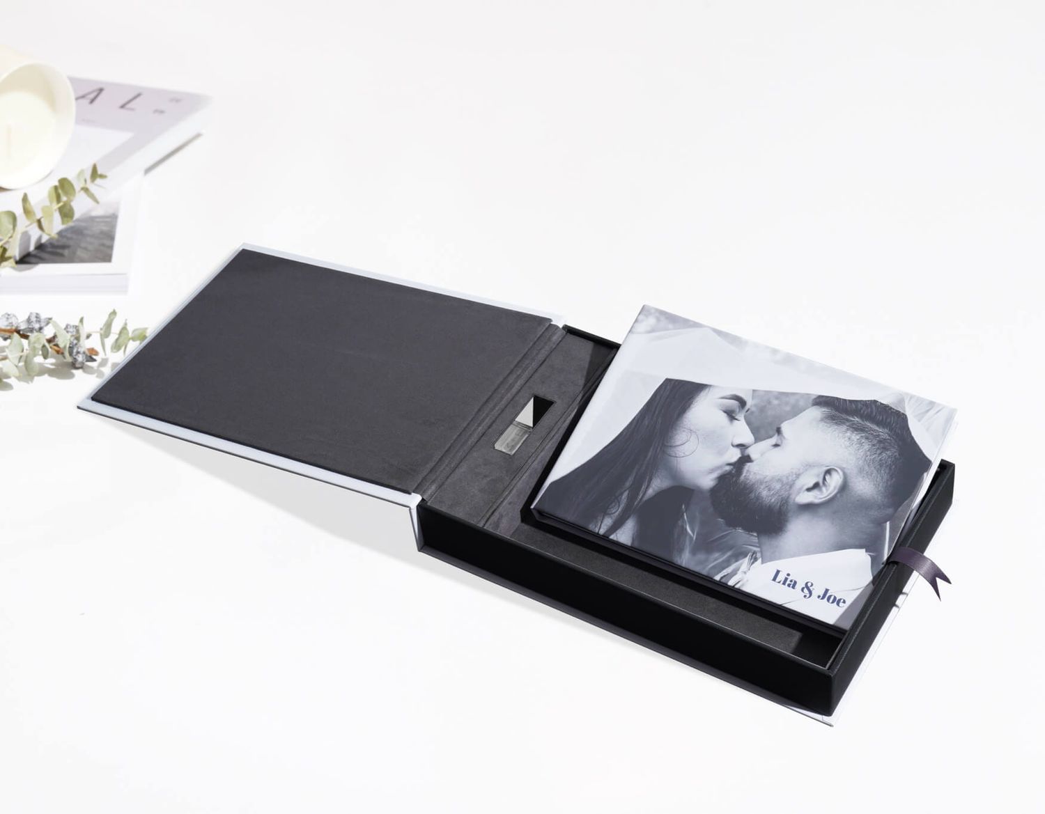 Elegant black leather photo album lying open with printed photos inside on white surface.