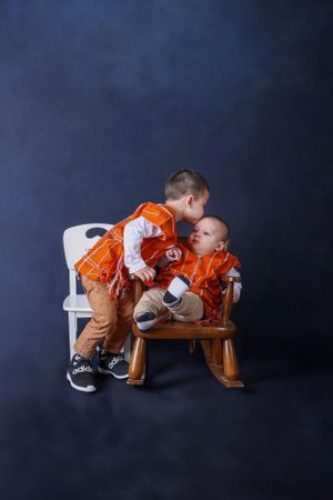 Two young brothers in matching orange outfits sharing a tender moment on a rocking chair.