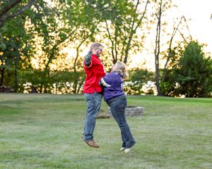 Couple dancing playfully outdoors on green grass at golden hour sunset in park.