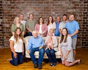 Multi-generational family portrait with elderly couple seated on sofa holding newborn baby.