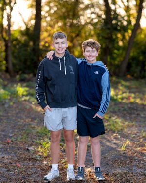 Two teenage brothers smiling with arms around each other in an autumn forest setting.