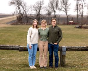 Two sisters and a brother posing casually outdoors on a farm with bare winter trees.