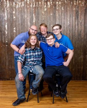 A family of five smiling together in front of a rustic wooden backdrop for a portrait.
