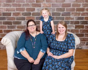 Two women and a young girl in matching floral outfits pose together on a white sofa.